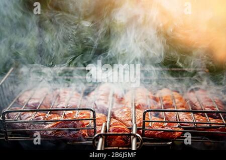 BBQ with fiery sausages on the grill. Raw sausages cevapcici grilled ha open fire on the street. Selective focus. Stock Photo