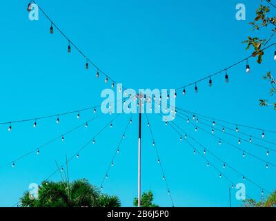 String wired bulbs from the pole in outdoor garden on blue sky background. Stock Photo