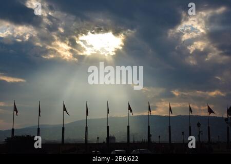 Sunlight coming through hole in clouds over flagpoles Stock Photo