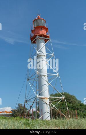 Landscape of lighthouse with red top and white base with green grass and blue sky background. Pape Lighthouse. Stock Photo