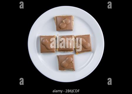 Five pieces of chocolate on a white plate isolated on a black background Stock Photo