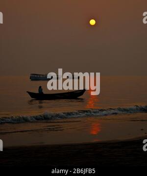 A day is ending as sun is setting on Bay of Bengal and  a tiny fishing  boat is passing through the shadow. Some other fishing boat is going to port. Stock Photo