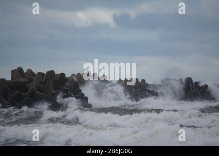 Waves crashing against breakwater consisting of gray concrete tetrapods. Liepaja, Latvia. Stock Photo