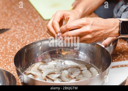 Woman chef in apron cleanse and cuts prawn with knife on kitchen table, seafood preparation recipe concept Stock Photo