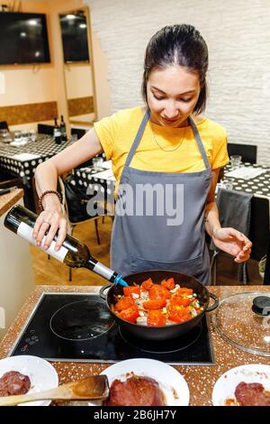 A woman cooking in the kitchen and pours a table wine or vinegar into the pan Stock Photo
