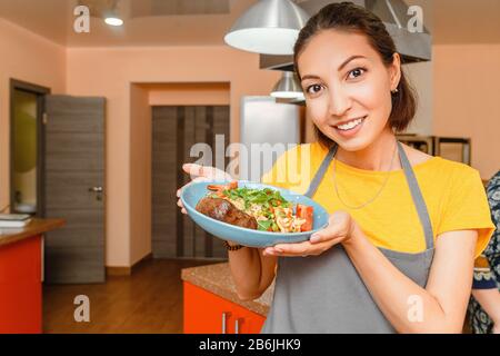 Pretty young asian woman wearing apron making dinner cooking paella on a stove in kitchen Stock Photo