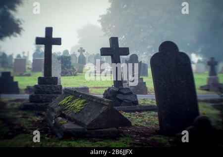 Misty view of dark stone crosses and tombstones in a deserted graveyard Stock Photo