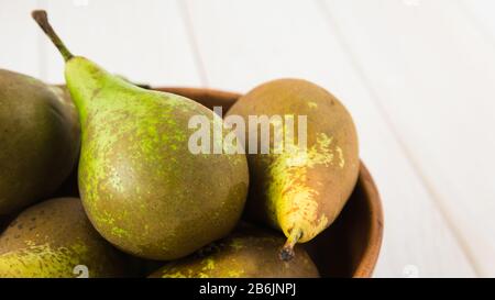 still life, green pears in a wooden plate on a white table, close-up Stock Photo