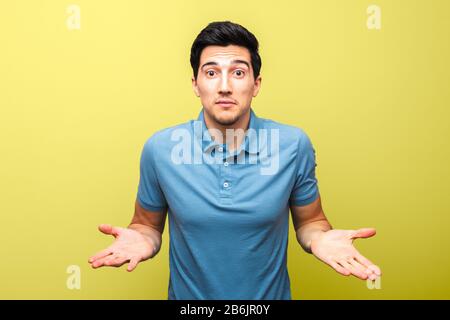 asking gesture of handsome man in blue shirt against yellow background. what is the matter Stock Photo