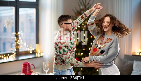 celebration, fun and holidays concept - happy couple wearing ugly sweaters dancing at christmas party Stock Photo