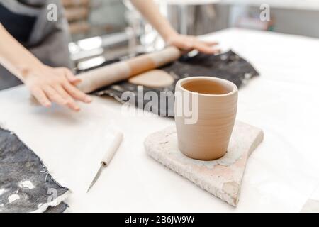 Close-up view of a female potter making and molding clay dishware in a workshop using different tools Stock Photo