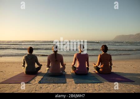 Rear view of women doing yoga at the beach Stock Photo