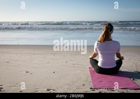 Rear view of woman doing yoga in front of the beach Stock Photo