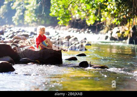Children hiking in Alps mountains crossing river. Kids play in water at mountain in Austria. Spring family vacation. Little boy on hike trail. Outdoor Stock Photo
