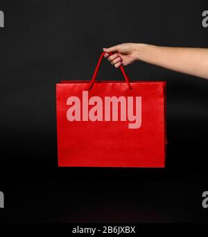 sale, consumerism and outlet concept - hand holding red shopping bag on black background Stock Photo