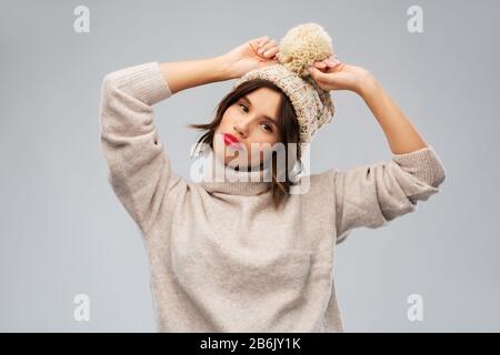 christmas, season and people concept - happy smiling young woman in knitted winter hat and sweater over grey background Stock Photo