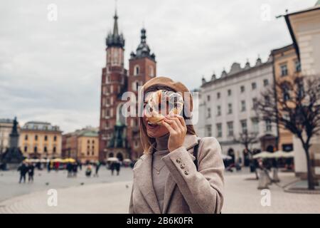 Tourist woman holding bagel obwarzanek traditional polish cuisine snack on Market square in Krakow. Travel Europe Stock Photo