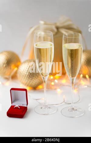 christmas, holidays and celebration concept - glasses of champagne and diamond ring in little red gift box Stock Photo
