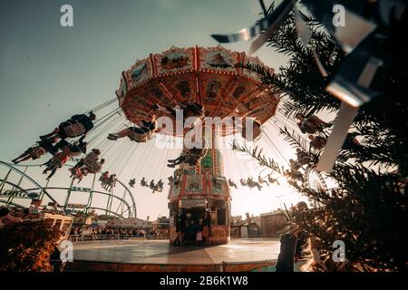 The sun is bright one the Oktoberfest fairground in Munich, Germany, with many people enjoying the carousel and rollercoaster rides after a beer. Stock Photo