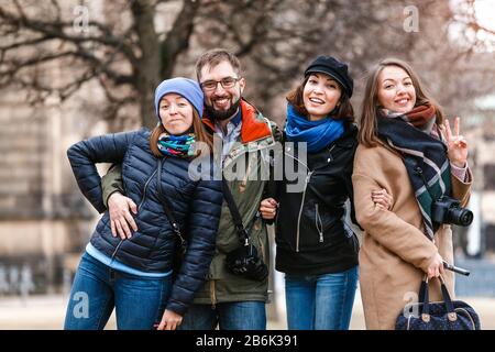 A team of four happy friends students hugs and laughs in the park of a European city in the winter, travel concept Stock Photo