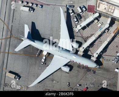 Qatar Airways Boeing 777 at Los Angeles (USA) Airport terminal connected to jet bridges for efficient boarding process. Inbound from Doha, Qatar. Stock Photo