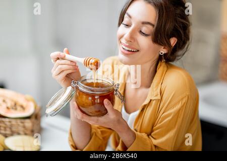 Portrait of a young and cheerful woman with a jar full of sweet honey on the kitchen at home Stock Photo