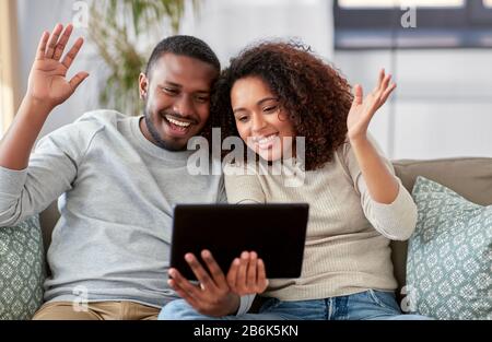 technology, internet and people concept - happy african american couple with tablet computer having video call at home Stock Photo