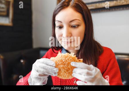 Woman's hands in gloves holding burger in modern fastfood restaurant Stock Photo