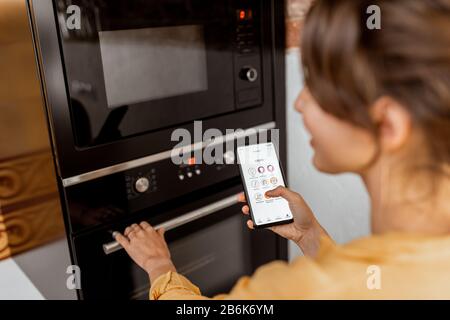 Woman controlling smart kitchen appliance using mobile phone at home, close-up on mobile screen. Concept of a smart home and managing home with mobile devices Stock Photo