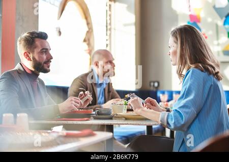 Bearded businessman sitting at table in restaurant and talking to colleague while having lunch Stock Photo