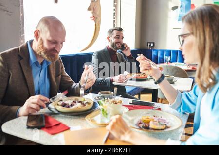 Business people in cafe: successful young businessman eating salad and discussing business on phone while colleagues having lunch together Stock Photo