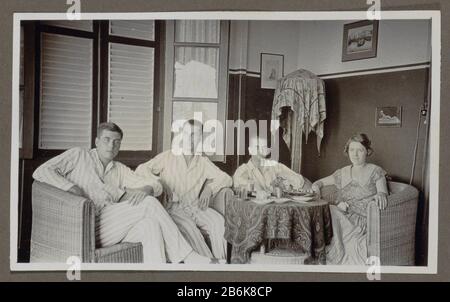 Three men and a woman around a table Three men in pajamas and a woman sitting in wicker chairs in the corner of a room. The shutters are opened partially. On the table are flowers, bowls and glasses. In the corner a standing lamp chamber. On the walls hang framed pictures of a cat, a face port and a sculpture of a lying child. Part of Family Album Dutch-Indië. Manufacturer : Photographer: anonymous Date: 1920 - 1930 Physical features: gelatin silver print material: paper Technique: gelatin silver print Dimensions: H 65 mm × W 110 mm Subject: interior of the house where: Dutch East Indies Stock Photo