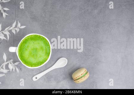 French almond cake makarons, white leaf, matcha tea in white cup with white spoon on concrete background Stock Photo