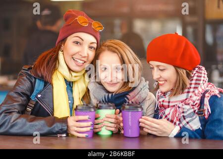 communication and friendship concept - smiling girls drinking coffee in outdoor cafe and smiling Stock Photo