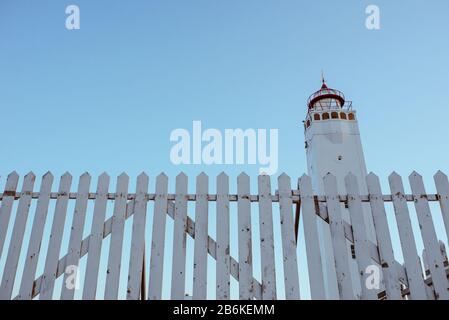 white lighthouse with white fence on blue sky background near the sea Stock Photo