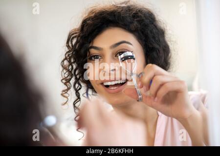 Beautiful dark-haired woman curling her eyelashes with a curler Stock Photo
