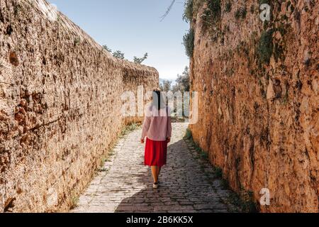 Young woman is walking between historical walls on a narrow alleyway. Tourism and Travel concept