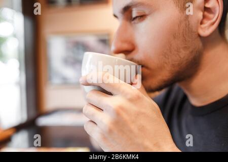 A young man in a cafe drinks his coffee or tea from a cup Stock Photo