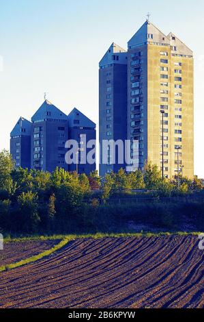 Freshly plowed field and residential buildings in background lit by setting sun. Urbanism, agriculture and sustainability concepts Stock Photo