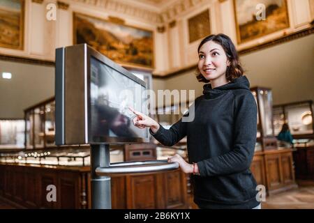 A woman in the museum uses the touchscreen monitor electronic guide, the concept of modern education Stock Photo