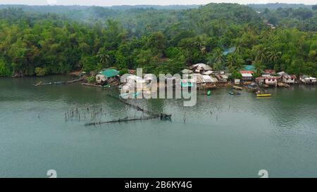 Fishing village with boats and slums with wooden houses, aerial drone. Houses community standing in water in fishing village. Luzon, Philippines. Stock Photo