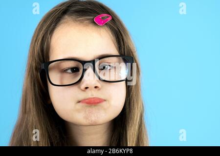 Close up portrait of a cross eyed child school girl wearing looking glasses isolated on blue background. Stock Photo