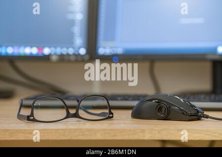 Closeup of protective glasses on an empty desk with blurred computer screen on background. Stock Photo