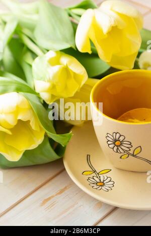 yellow tulips, pastel yellow cup of tea with lemon on a white shabby wooden background. Vertical Stock Photo