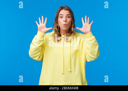 Imagine this. Excited and happy outgoing blond girl explain something and gesturing, holding hands near face, showing number ten, talking to camera Stock Photo