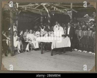 Feestelijke bijeenkomst met Nederlanders en Surinamers Festive meeting with Dutch and Surinamese. Three men standing at a table, left in the first row Edith Jetten in a chair, right a few scouts. Photo with corners attached to a page of an album leaf in the photo album on the family Jetten and li and working in the mining town of Moengo in Suriname around 1927. Manufacturer : Photographer: anonymous place manufacture: Suriname Date: 1925 - 1927 Material: paper Technique: Photography Dimensions: h 131 mm × W 176 mm Subject: anonymous historical persons Portrayed in a group, in a group-portrait Stock Photo
