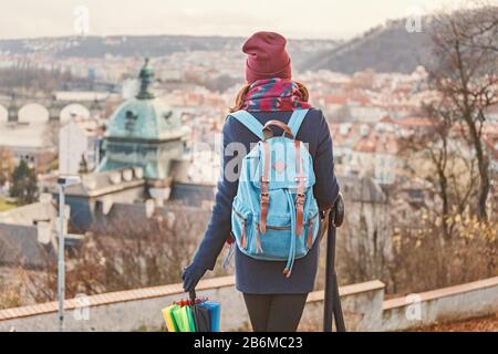 Woman tourist in a coat with a backpack travels in the city park of Prague, rear view Stock Photo