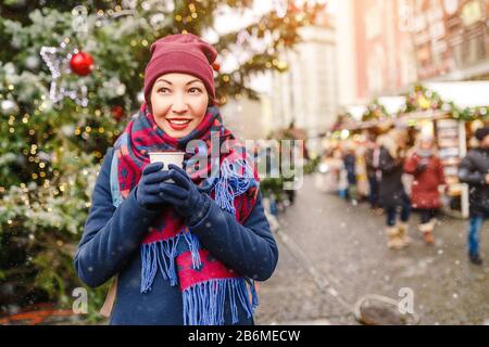 Young woman at Christmas fair drinking hot drink at New Year tree background Stock Photo