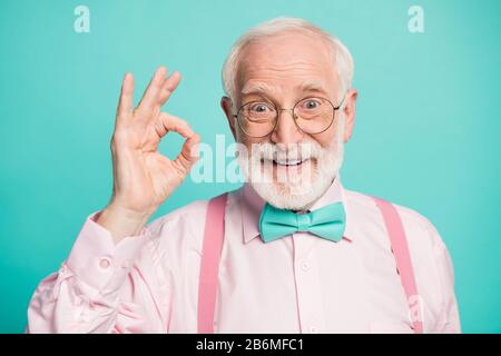 Closeup photo of amazing grey haired grandpa showing okey symbol express agreement wear specs pink shirt suspenders bow tie isolated bright teal color Stock Photo