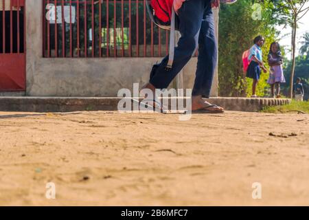 African boy in flip flops and backpack coming back from school with two girl  schoolmates in the background, Matola, Mozambique Stock Photo